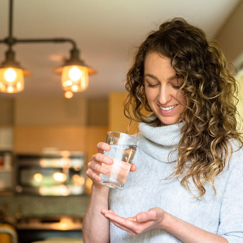 Woman holding a glass of water and looking at sugar-free functional mushroom extract capsules in her hand