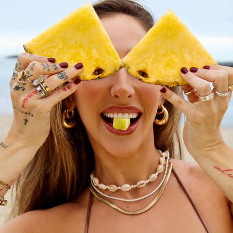 Woman holding pineapple slices over her eyes with a yellow Road Trip pineapple mushroom gummy on her tongue
