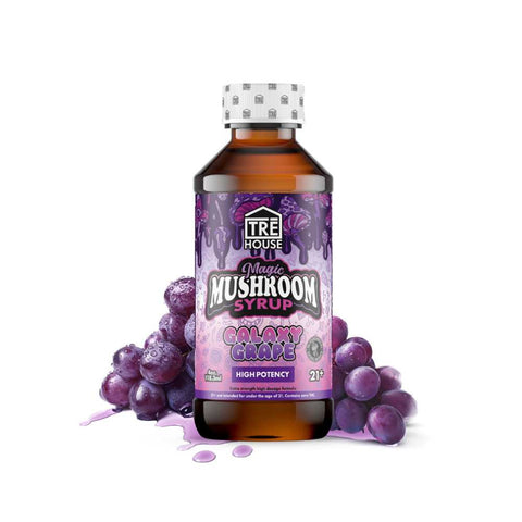 A bottle of Tre House Magic Mushroom Syrup with a label indicating Galaxy Grape flavor. The bottle is placed against a white background with a spray of purple grapes in front of it, suggesting the flavor of the syrup.